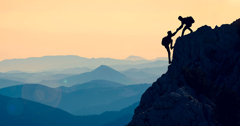 hikers helping each other up a mountain